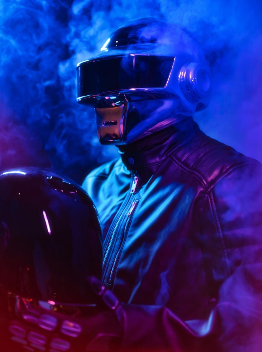 A man wears a Guy-Manuel Daft Punk helmet in a room with neon lights and smoke